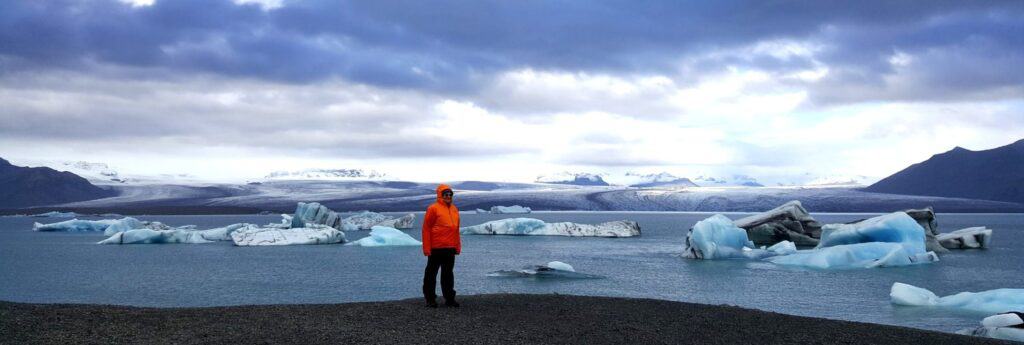 woman standing on a black beach in front of the glacier lagoon