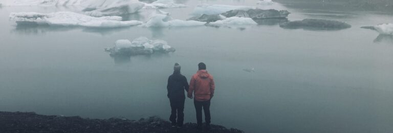 man and woman holding hands looking at lake