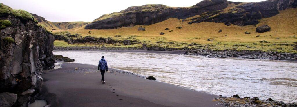 Man walking on a black sand beach next to a lake in Iceland