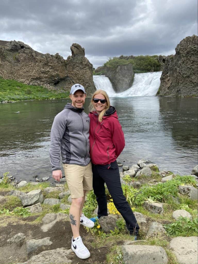 man and woman stanig in front of lake and waterfall