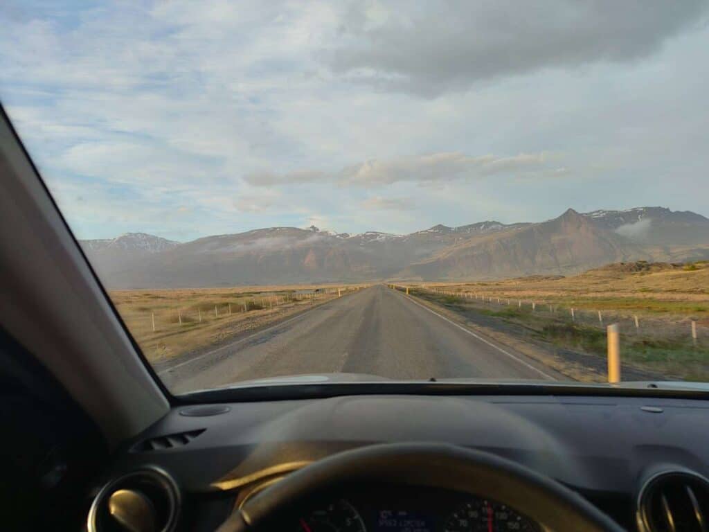 Looking out the front windshield of a car onto an open paved road with grass on either side.