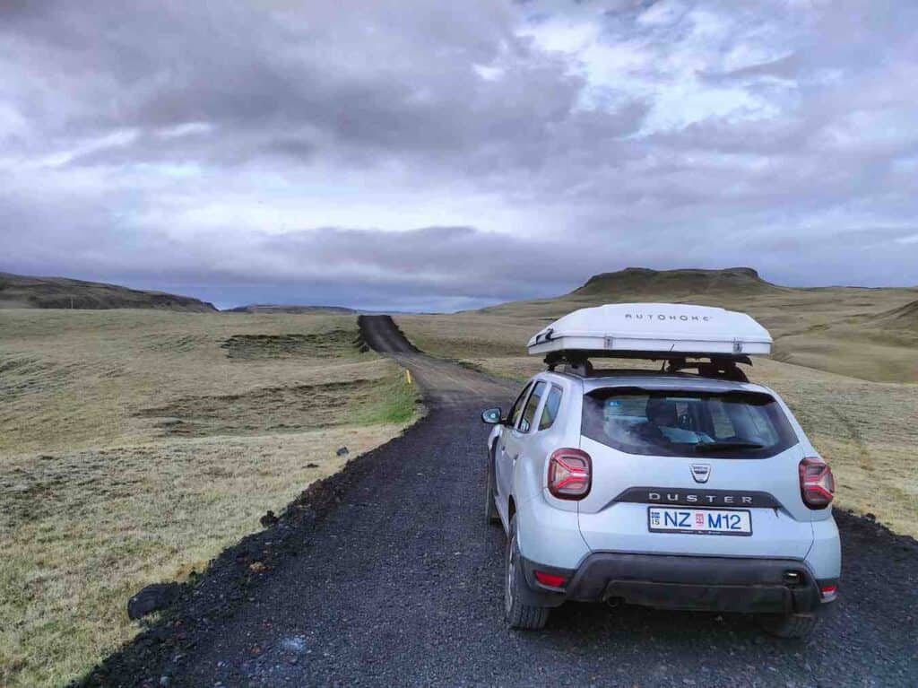 A Dacia Duster with a closed rooftent, parked on a gravel path heading far.