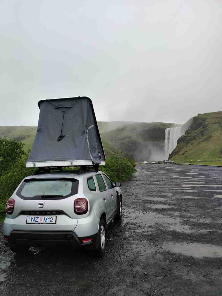 Dacia Duster with open roof tent, camped infront of the watterfall Skógarfoss in the rain.