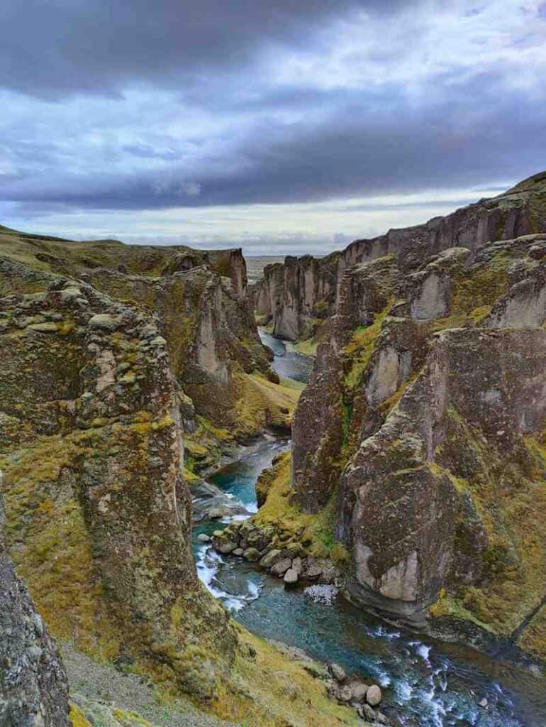 A river running through tall rocky walls with moss.