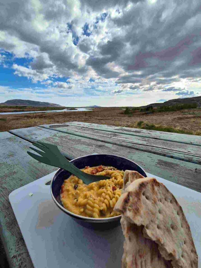 A bowl with mac and cheese located on a table. Bread on the side