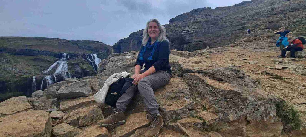 A woman sitting on rocks posing next to a small waterfall.