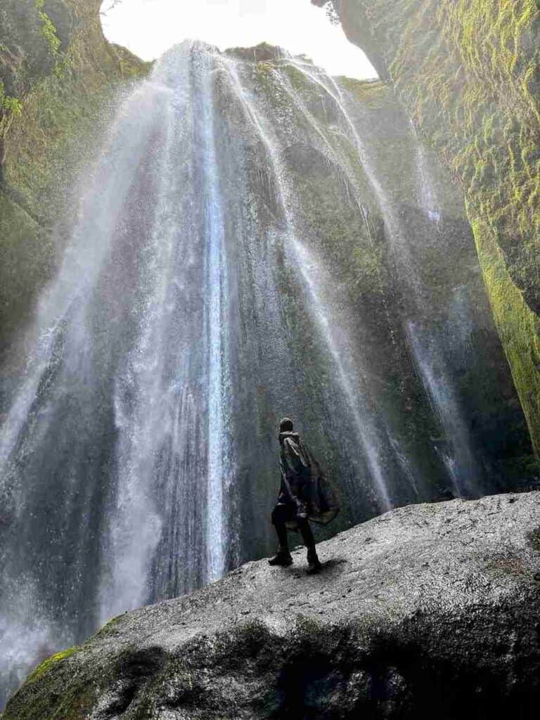 A man in a rain poncho looking up at the Gljúfrabúi waterfall
