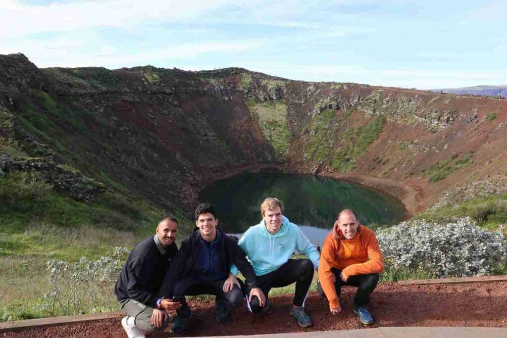 Four guys crouching down by a crater with water.