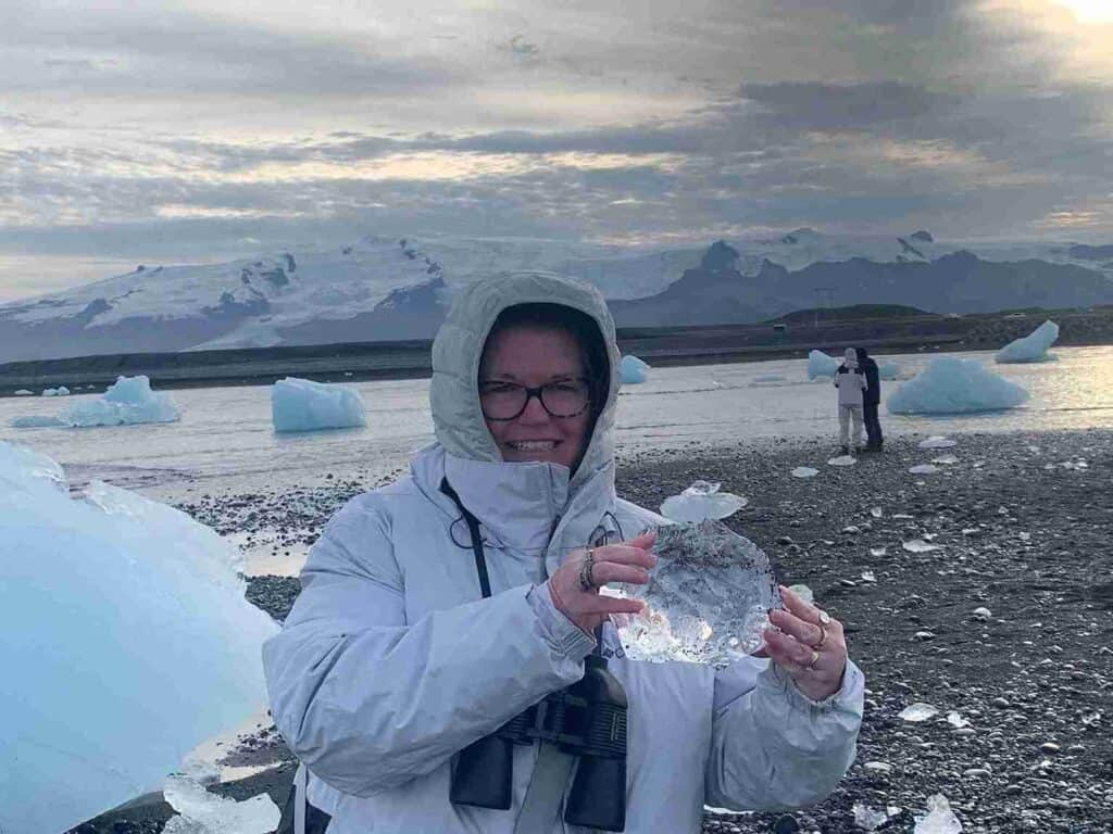 A woman with glasses holding a large piece of Ice by Jökulsárlón (glacier lagoon)