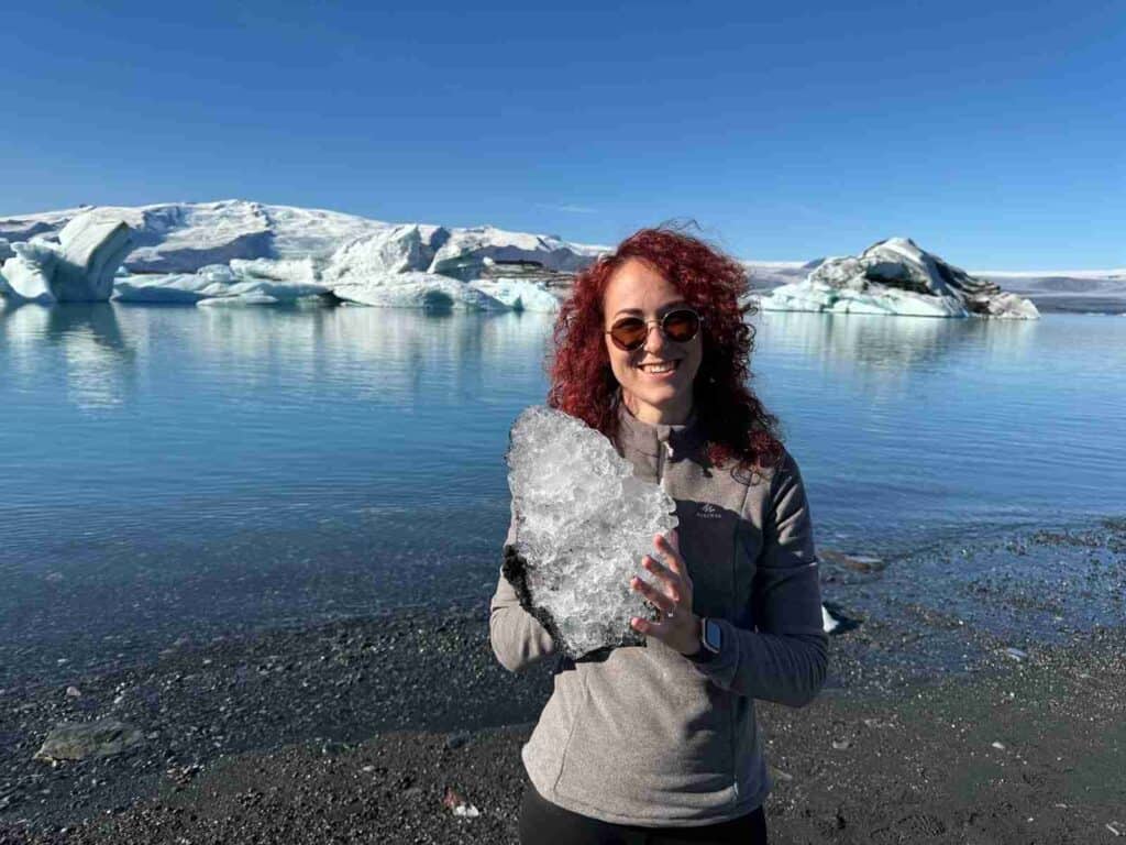 A woman standing by the glacier lagoon holding a small ice rock