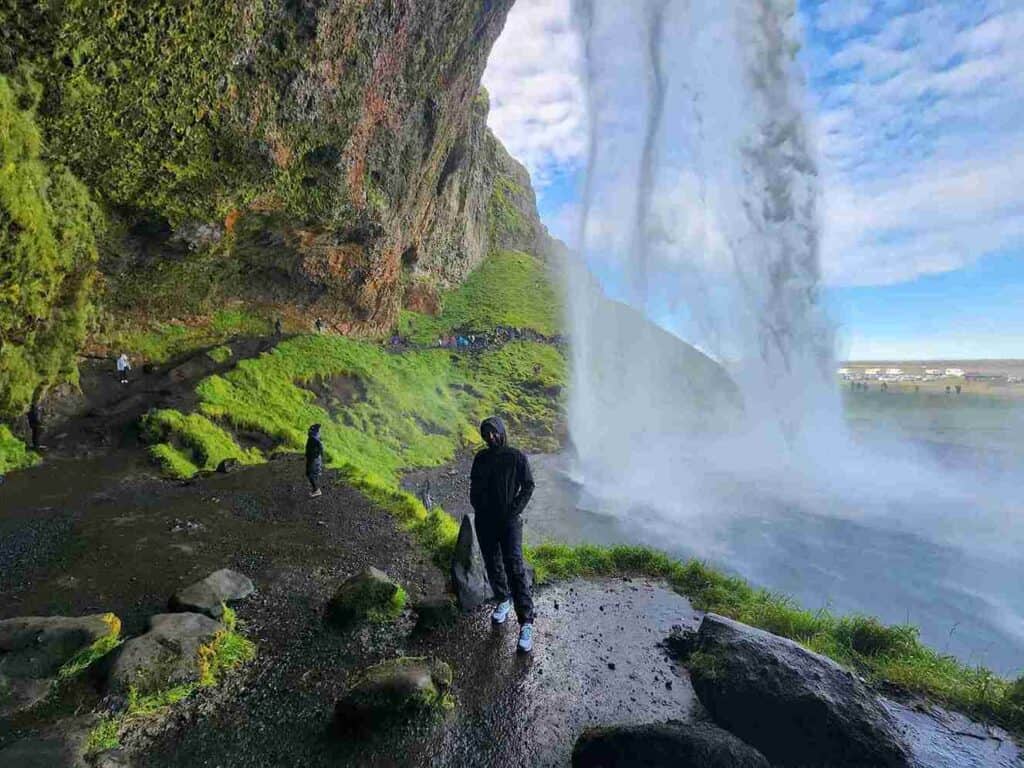 A woman standing behind Seljalandsfoss waterfall.